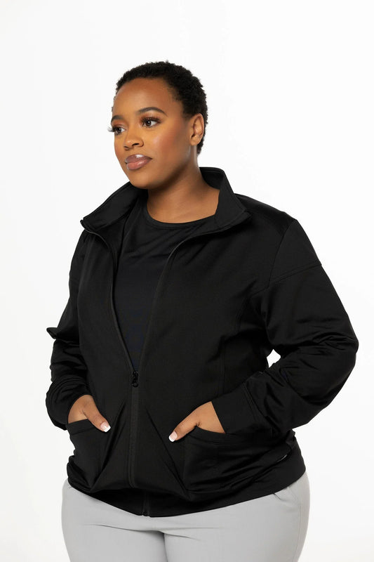 Woman wearing a black zip-up jacket with hands in pockets, posing against white background