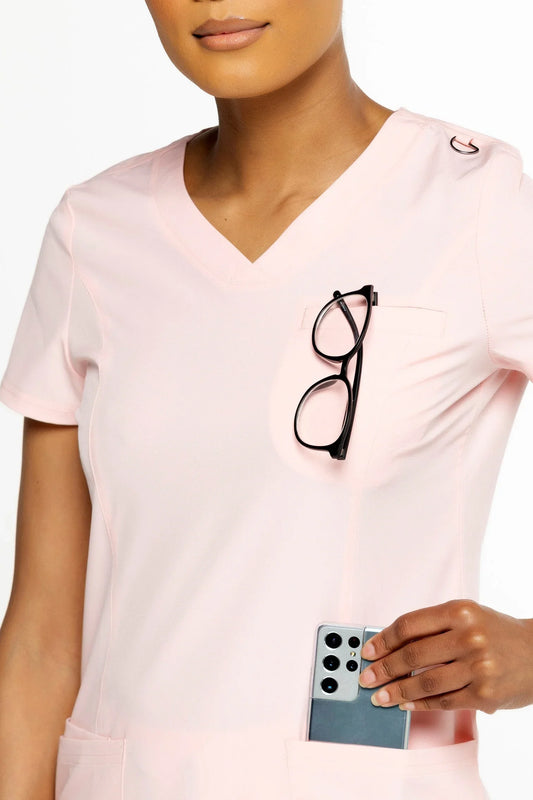 Woman wearing light pink medical scrub top with black eyeglasses in chest pocket and smartphone in lower pocket