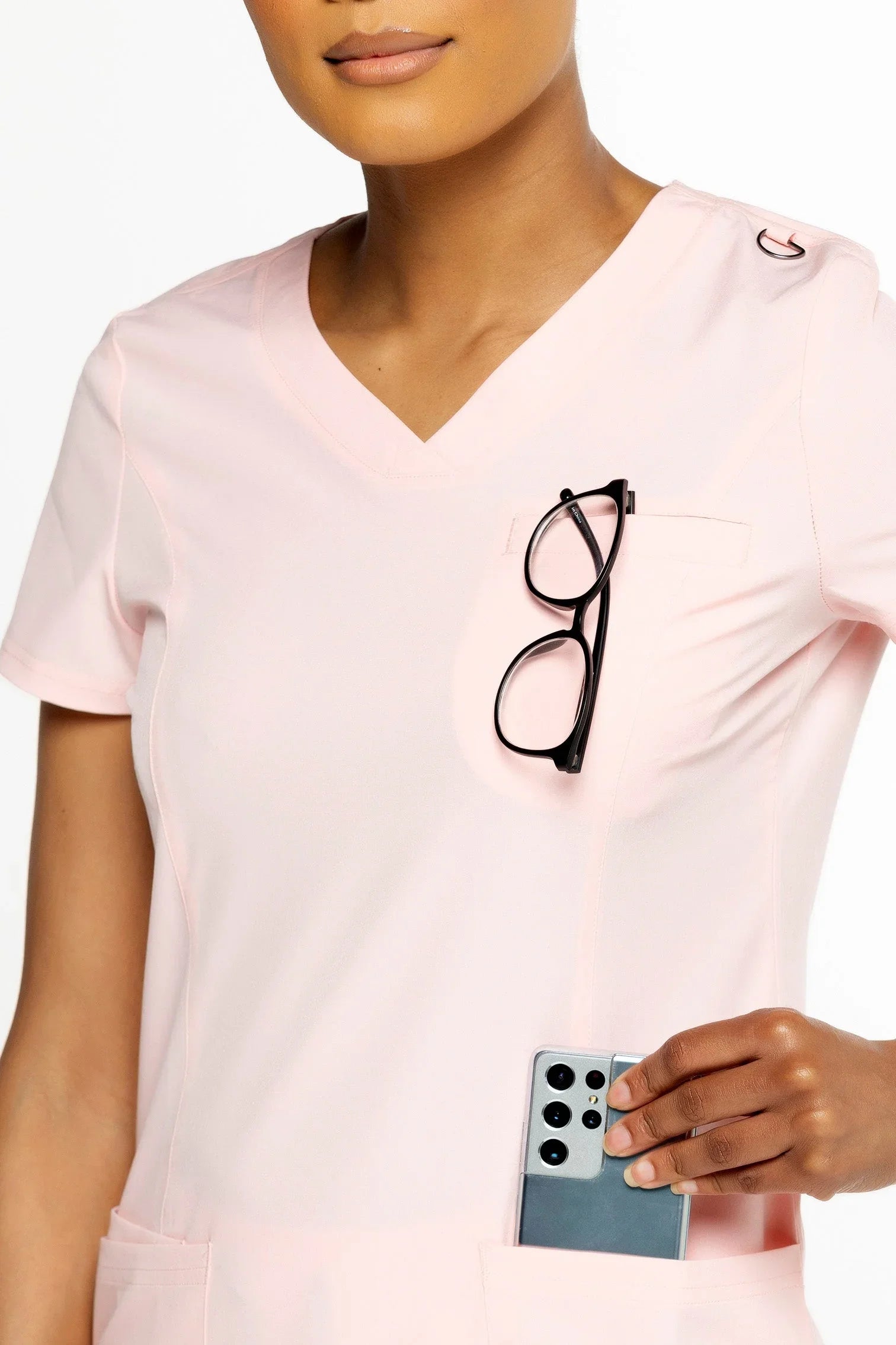 Close-up of woman in light pink medical scrub top with black glasses in chest pocket and smartphone in side pocket