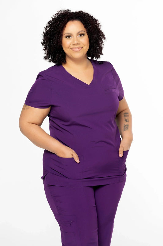 Plus size woman wearing purple medical scrubs with pockets on white background