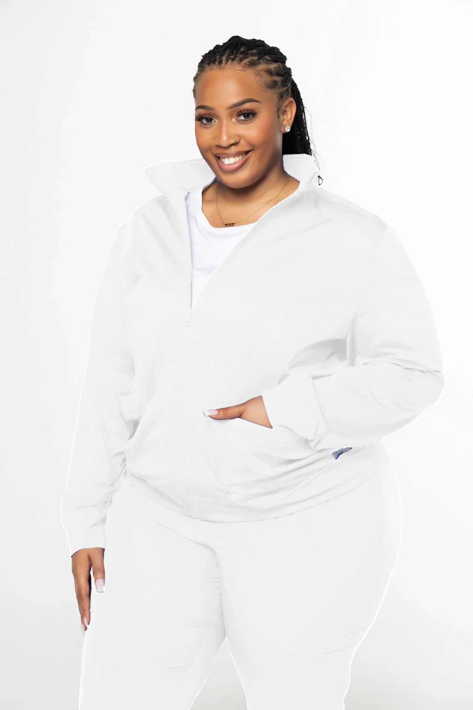 Smiling woman with braids wearing white zip-up jacket and pants, posing against white background