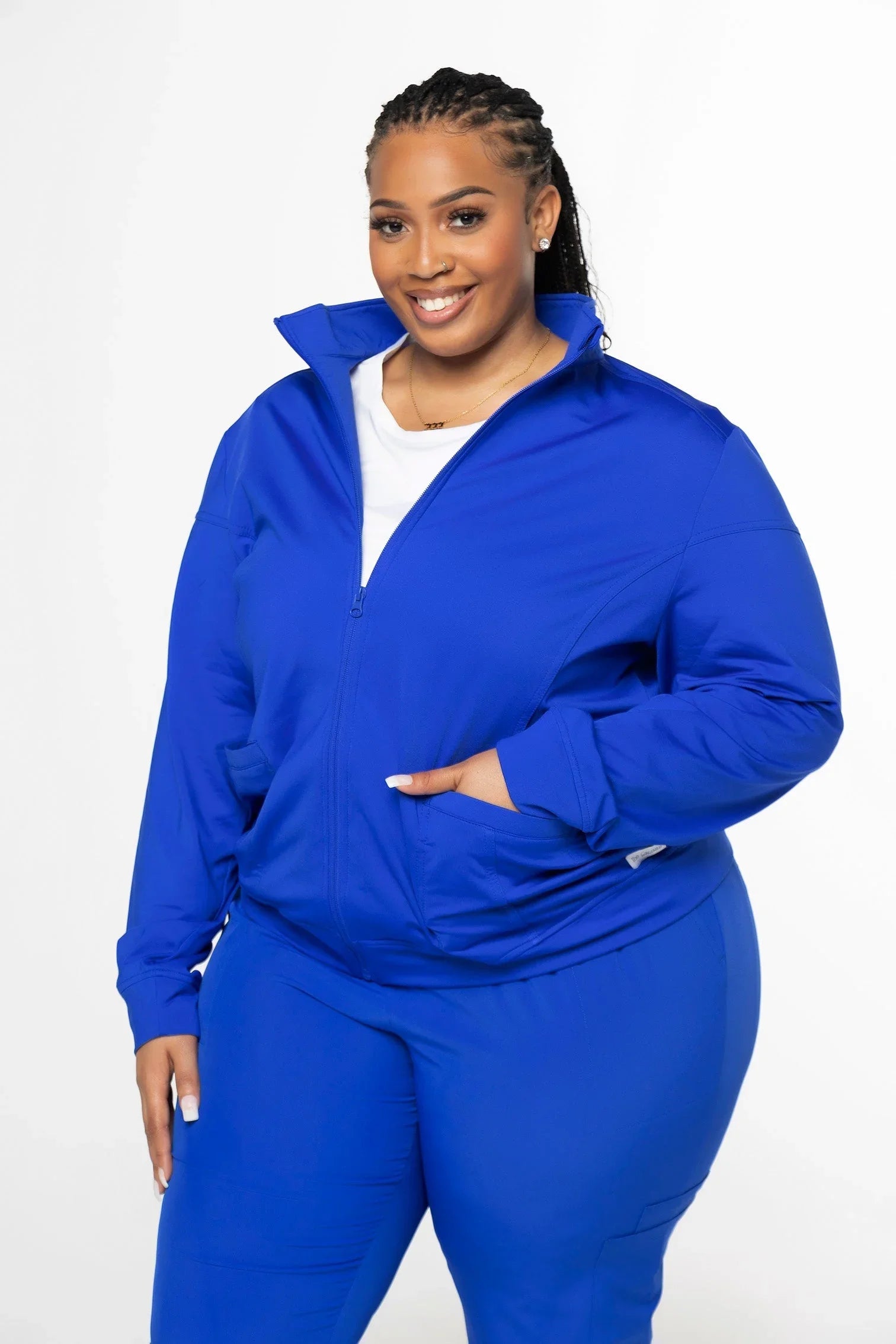 Smiling woman in royal blue zip-up jacket and matching pants, posing against white background