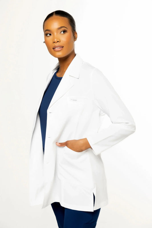 Female model wearing a white medical lab coat over navy blue scrubs with a white background