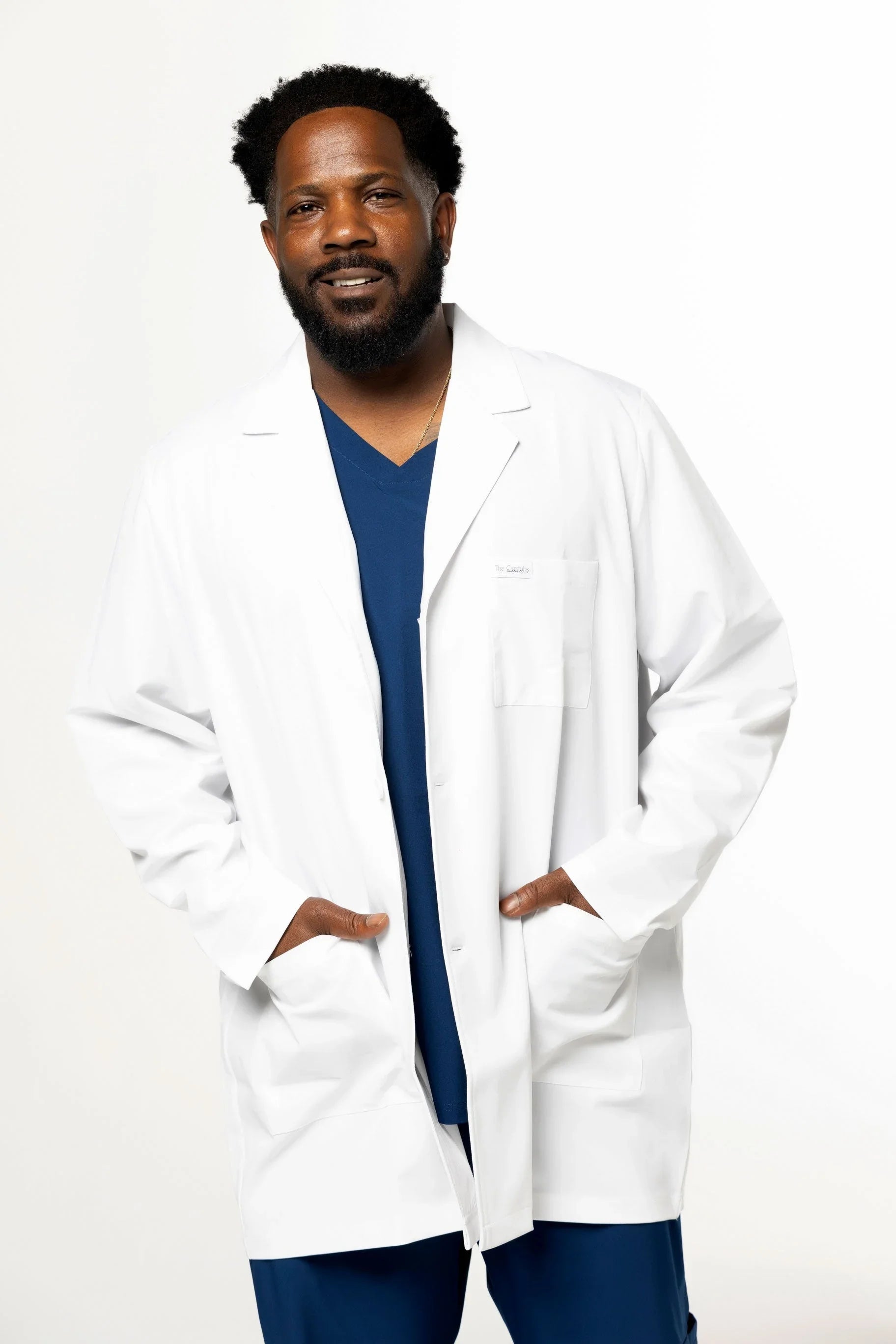 Smiling male healthcare professional in white lab coat and navy blue scrubs on white background