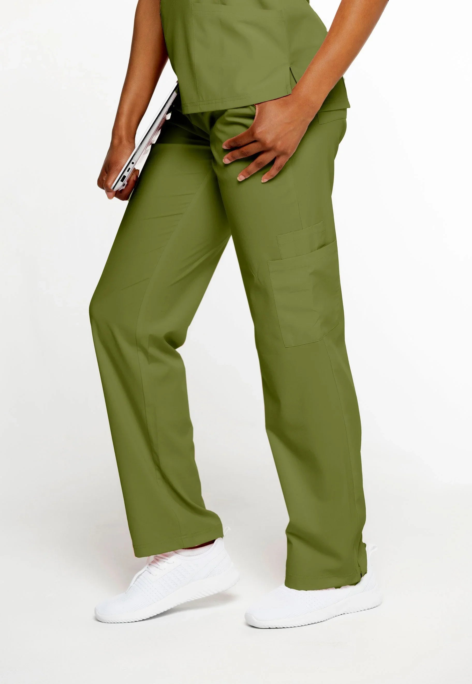 Person wearing green medical scrub pants with pockets and white sneakers, holding a closed laptop