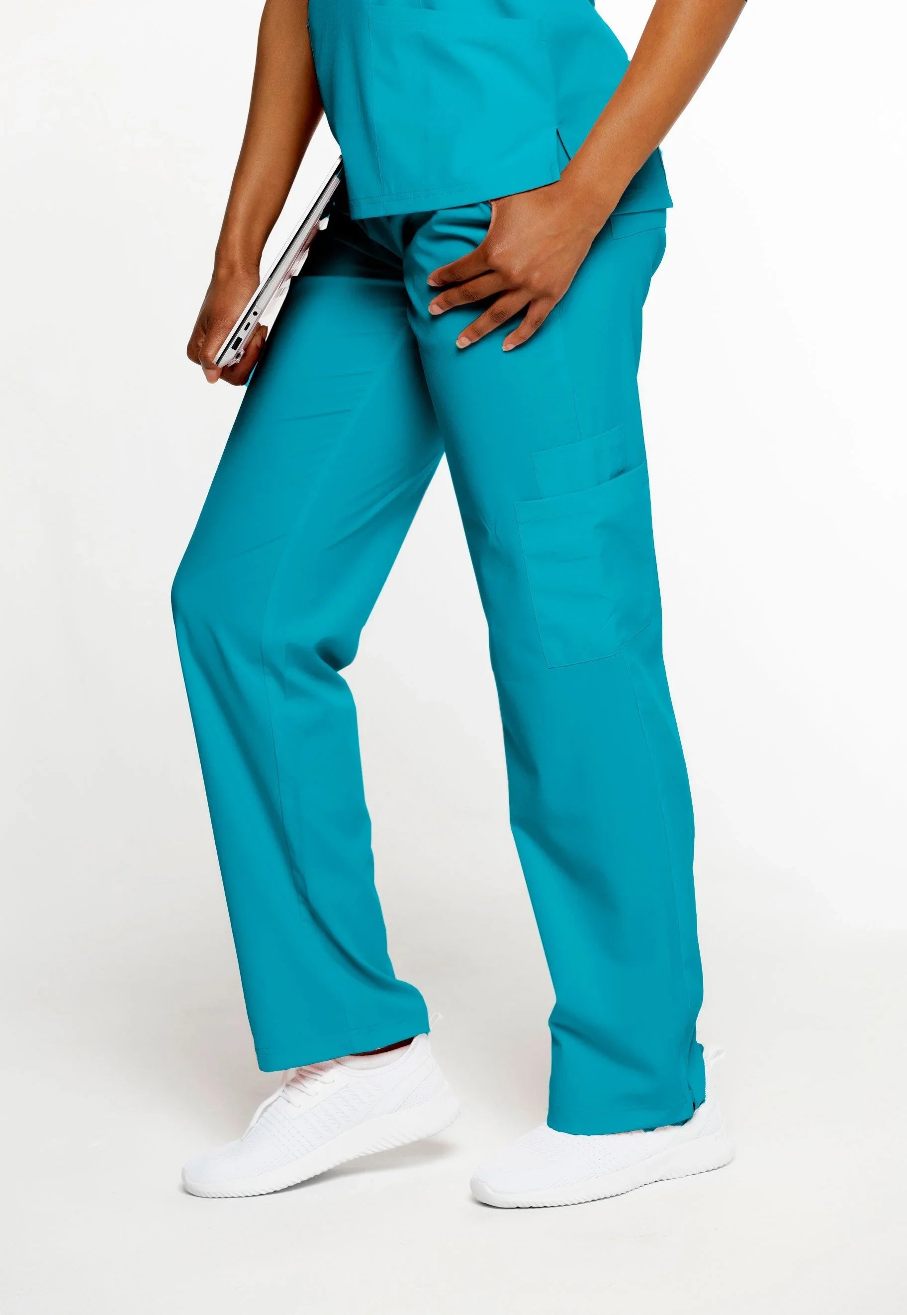 Person wearing teal medical scrubs pants with a cargo pocket and white sneakers holding a tablet
