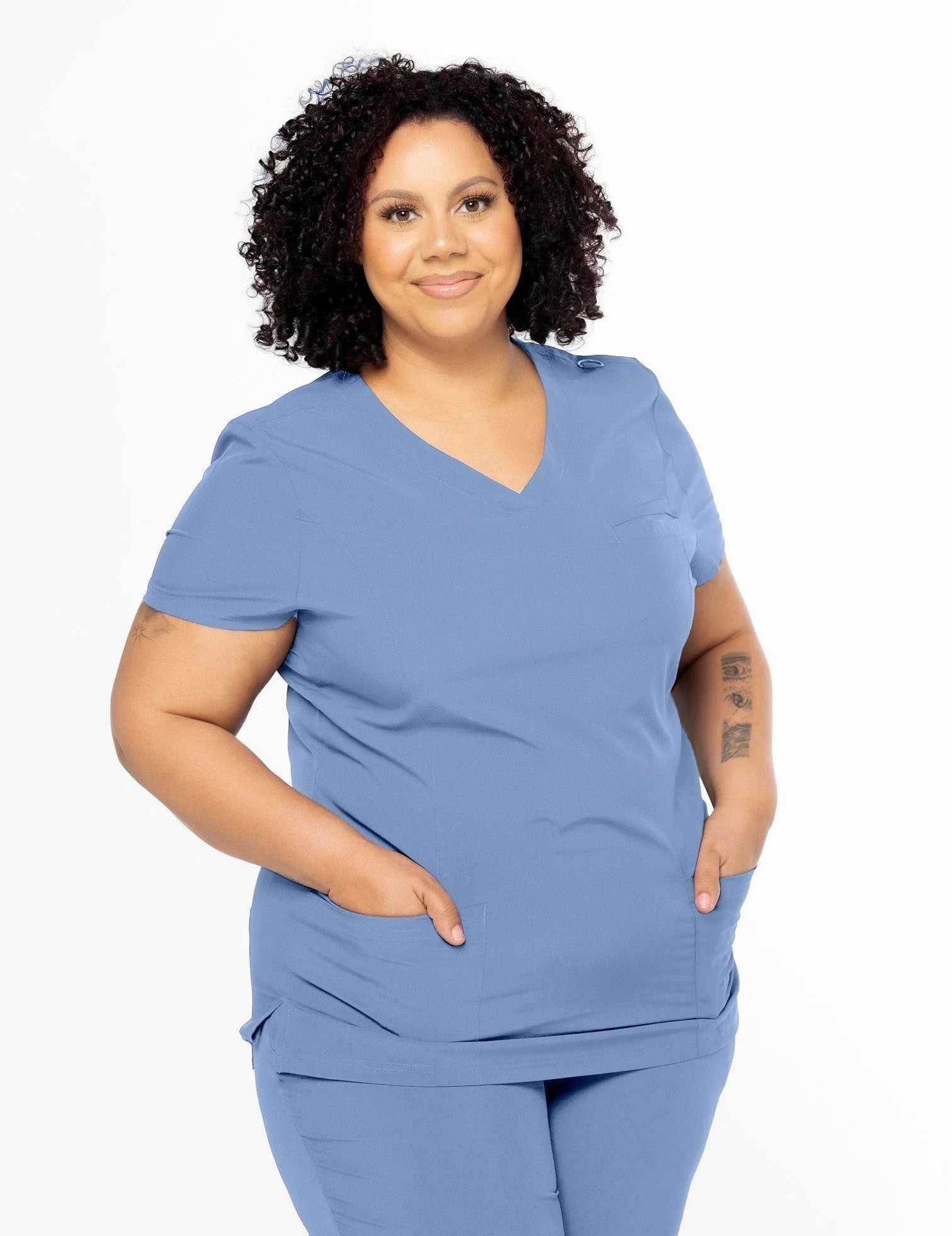 Confident plus-size woman wearing light blue medical scrubs with pockets on white background