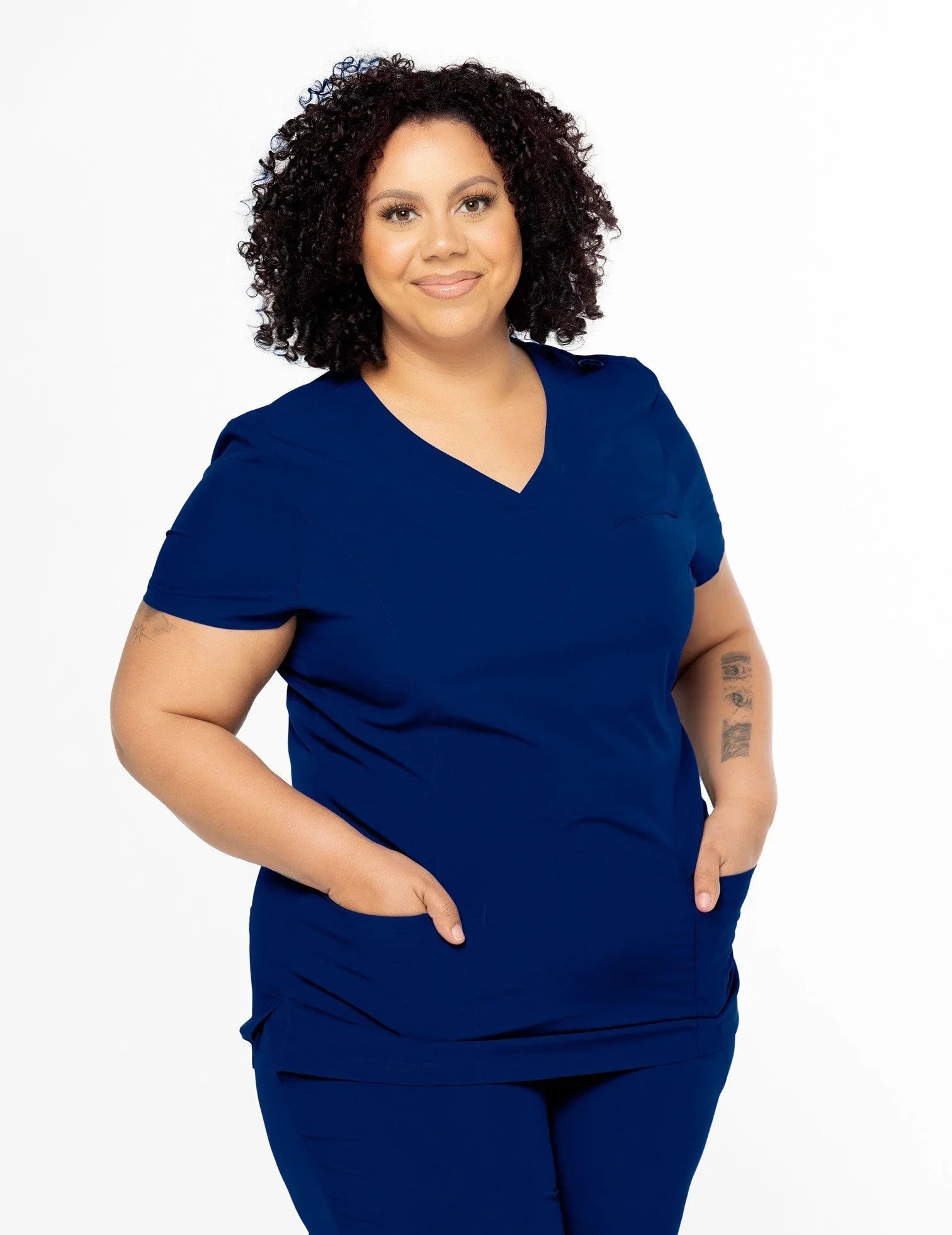 Curly-haired woman wearing navy blue medical scrubs with V-neck and pockets, smiling
