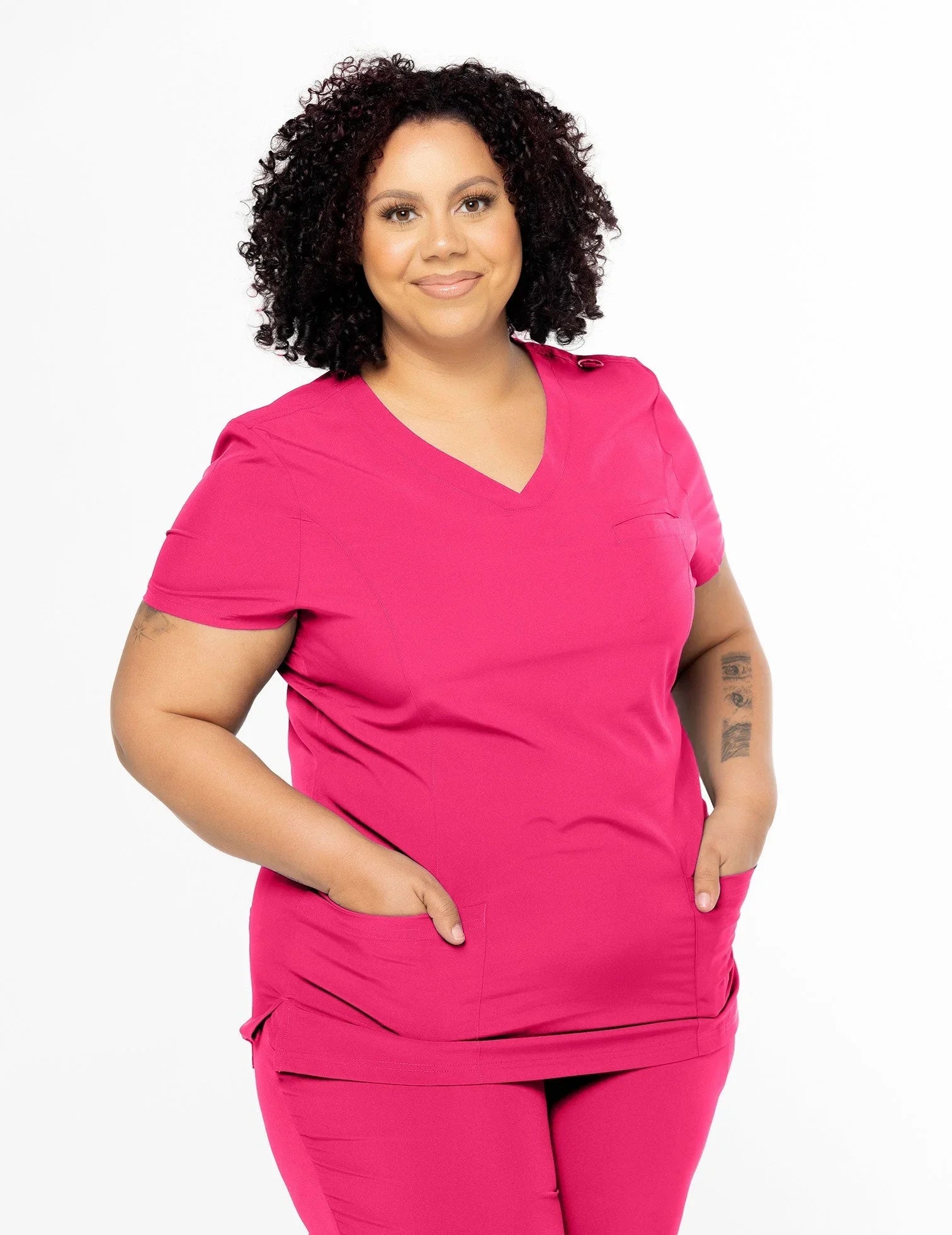 Plus size woman wearing hot pink medical scrubs with pockets, standing against white background