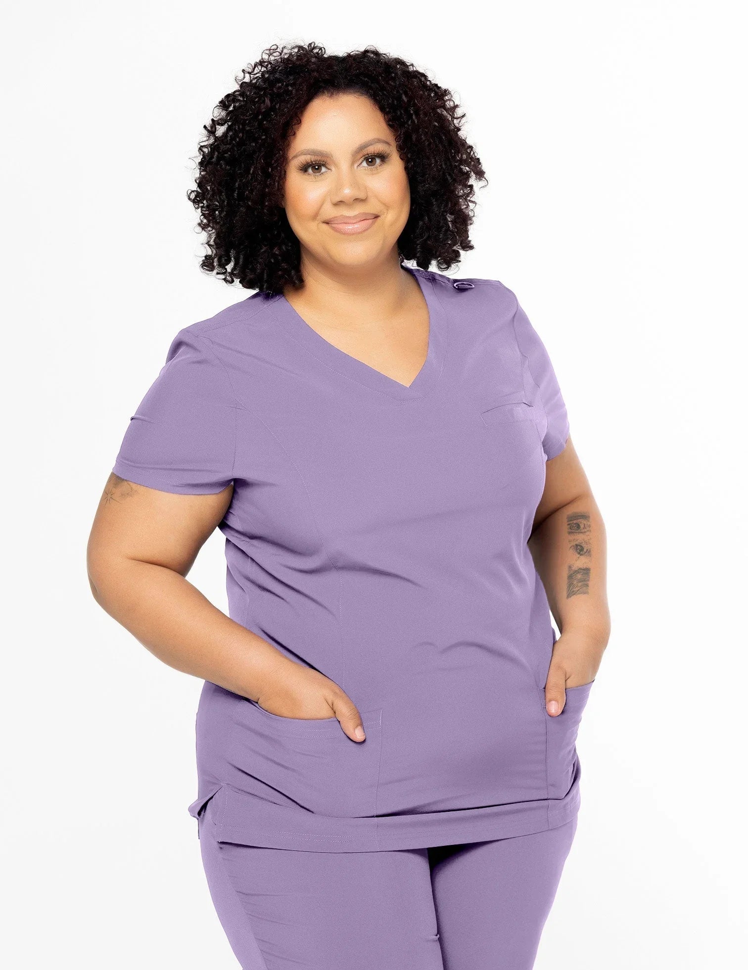 Plus size woman wearing lilac medical scrubs with pockets, smiling on white background