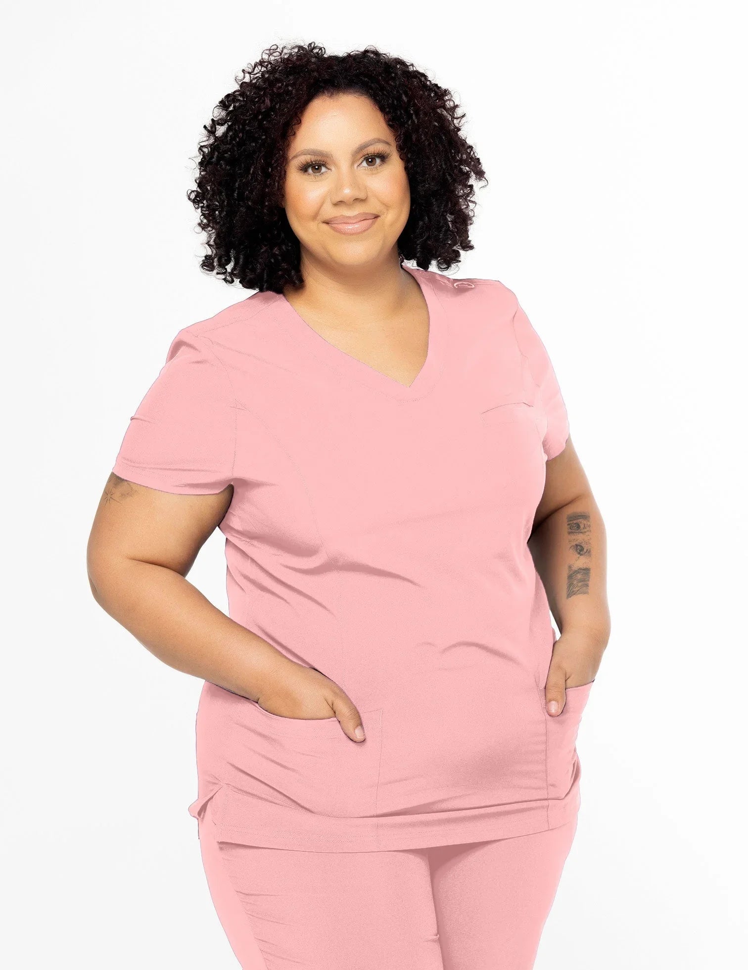 Confident woman wearing peach medical scrubs with pockets, standing against white background