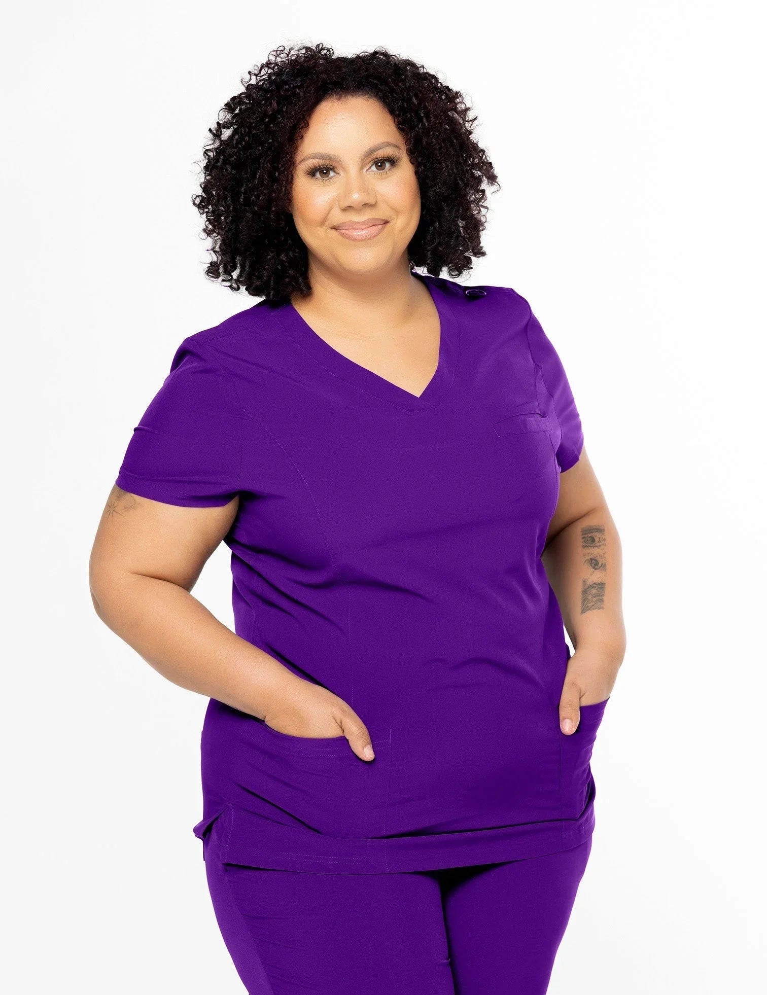 Plus size woman wearing purple V-neck medical scrubs with pockets on white background