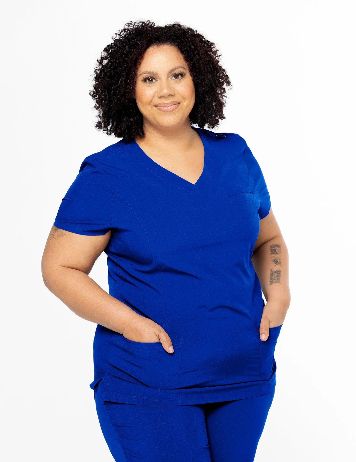 Confident woman wearing royal blue medical scrubs with V-neck and pockets, smiling, white background