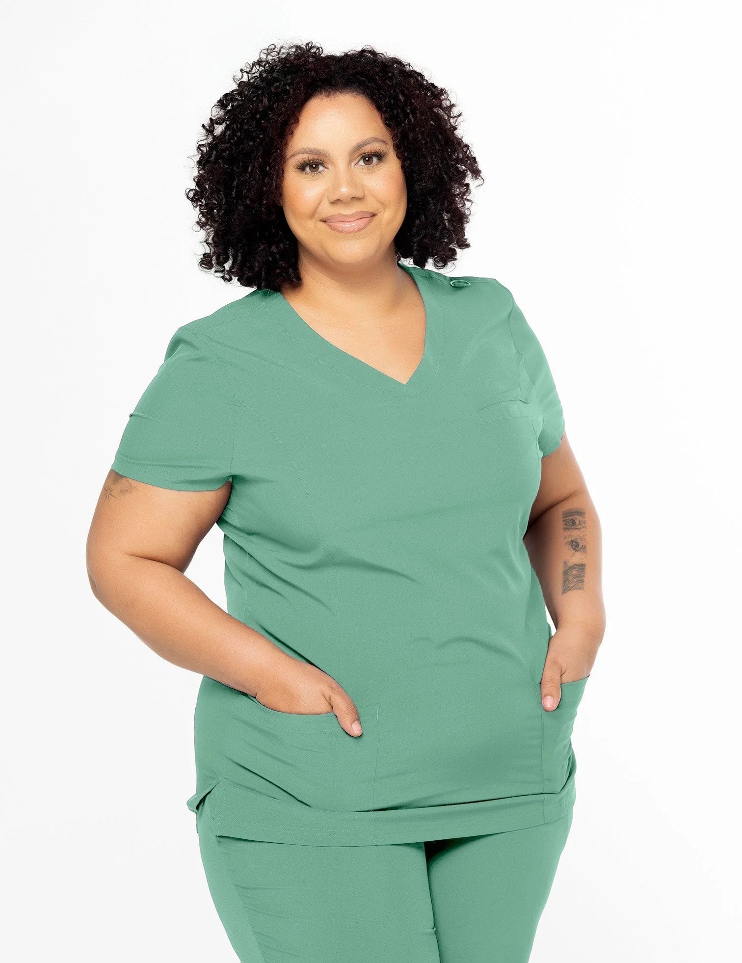 Smiling plus-size woman wearing sea green medical scrubs with hands in front pockets on white background