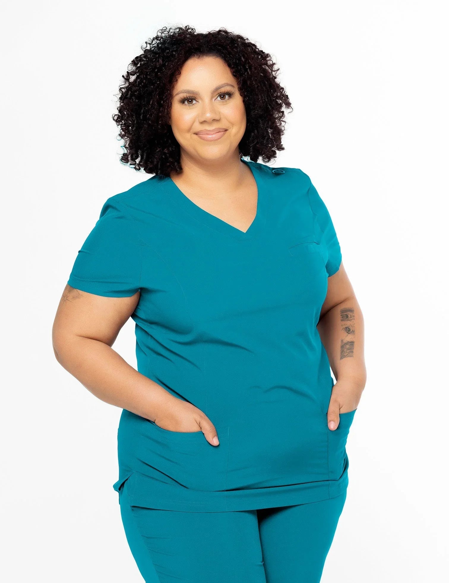 Smiling woman wearing teal medical scrubs with short curly hair and tattoos on arms