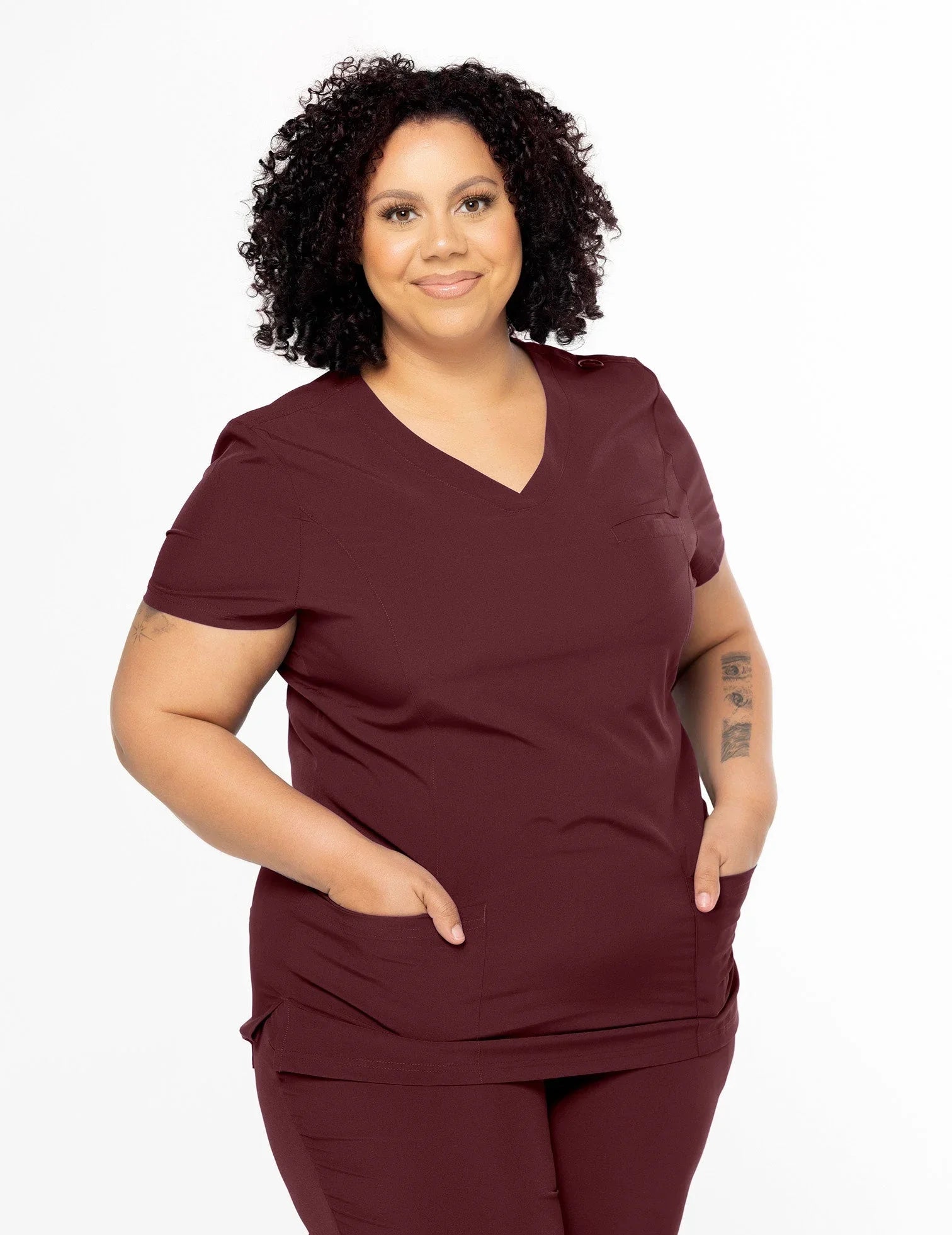 Smiling woman in wine-colored medical scrubs with pockets, standing against white background